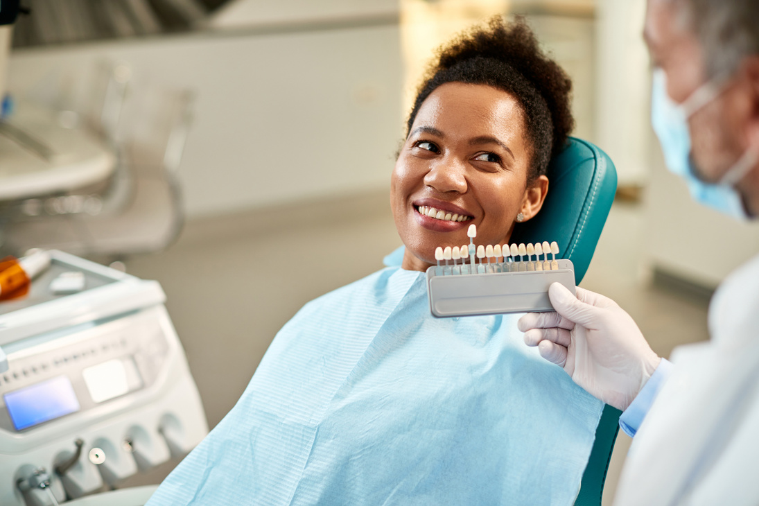 Happy black woman and her dentist choosing shade of dental veneers.